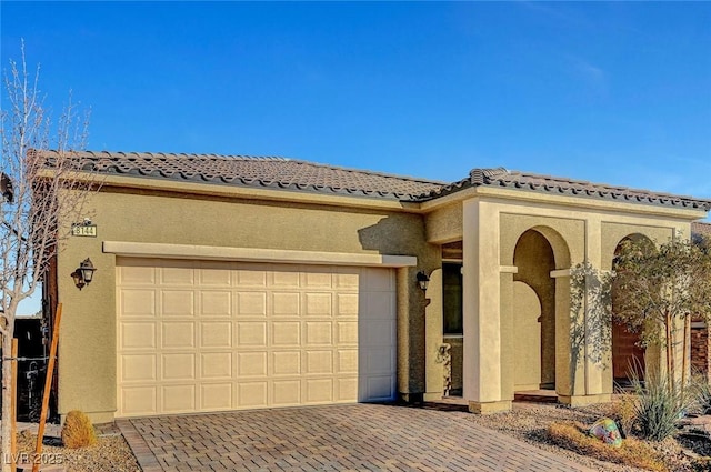 mediterranean / spanish house featuring a garage, decorative driveway, and stucco siding