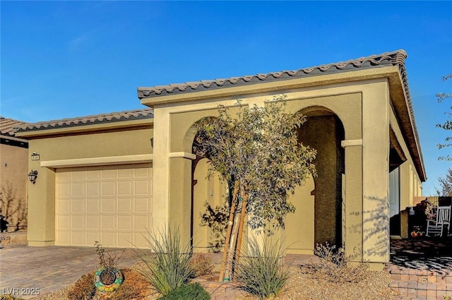 view of front facade featuring a garage, a tiled roof, decorative driveway, and stucco siding