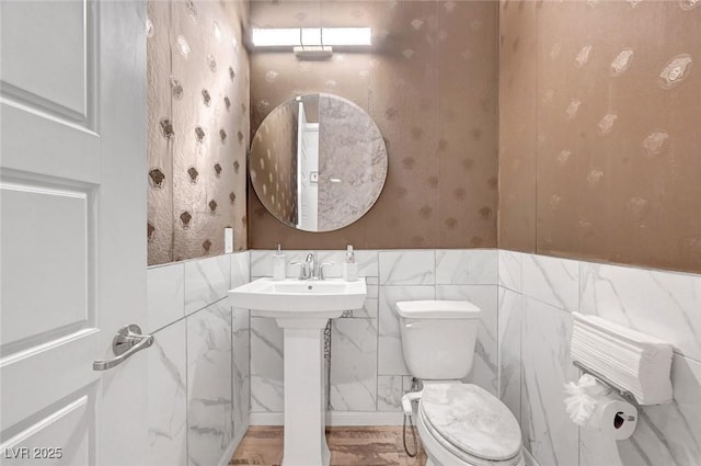 half bath featuring a wainscoted wall, a sink, toilet, and wallpapered walls