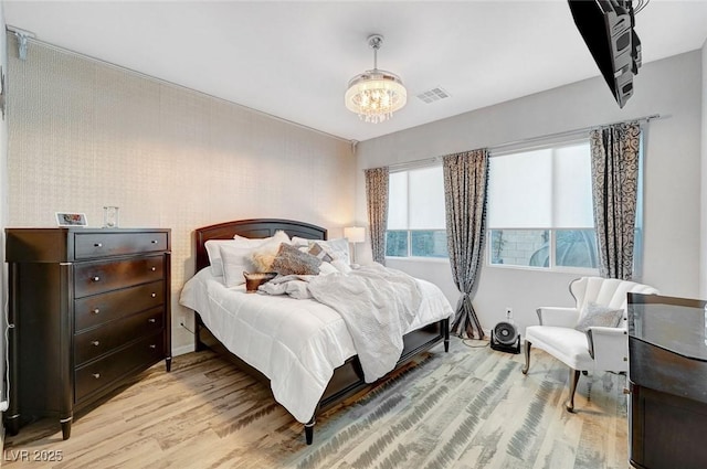 bedroom with wood finished floors, visible vents, and a notable chandelier