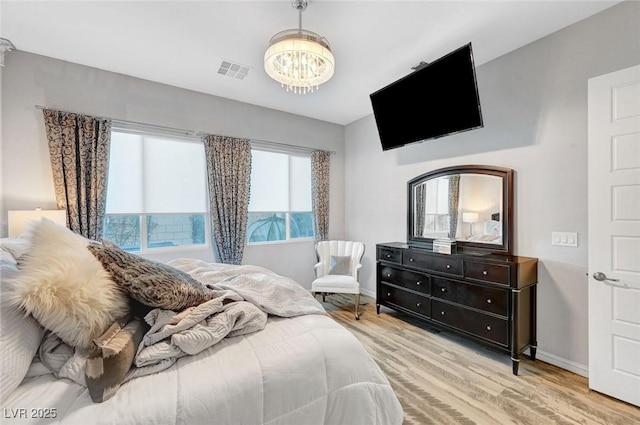 bedroom featuring baseboards, wood finished floors, visible vents, and an inviting chandelier