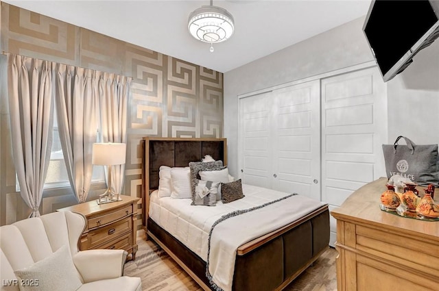 bedroom featuring wallpapered walls, light wood-style flooring, an accent wall, and a closet