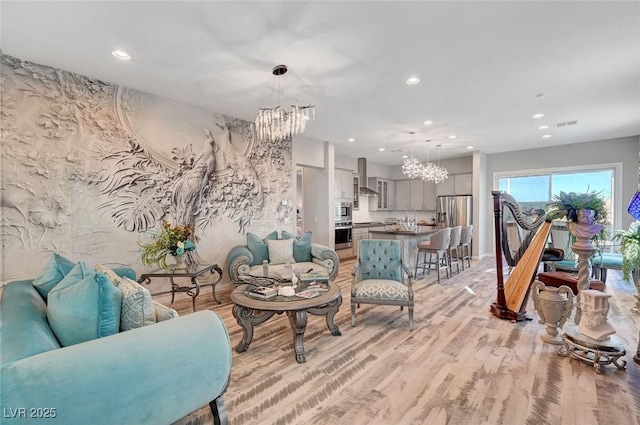 living area with light wood finished floors, recessed lighting, visible vents, and an inviting chandelier