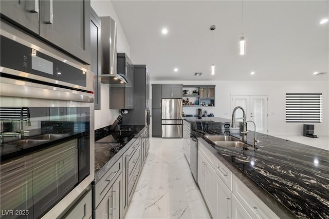 kitchen with dark stone counters, appliances with stainless steel finishes, marble finish floor, wall chimney range hood, and a sink