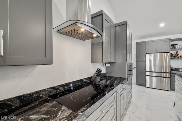 kitchen featuring marble finish floor, gray cabinets, freestanding refrigerator, wall chimney exhaust hood, and black electric cooktop