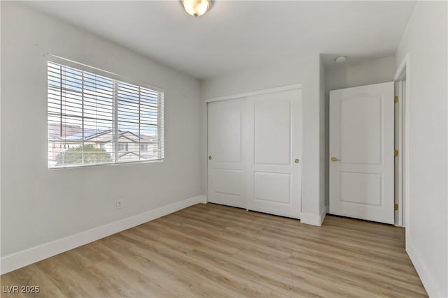 unfurnished bedroom featuring light wood finished floors, baseboards, and a closet