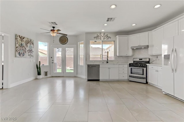 kitchen with under cabinet range hood, white cabinets, light countertops, appliances with stainless steel finishes, and tasteful backsplash