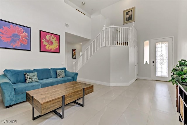 living area with stairs, a high ceiling, visible vents, and baseboards