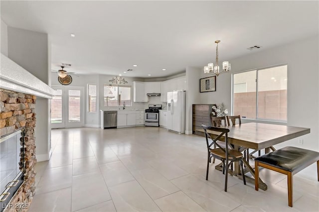 dining room featuring visible vents, baseboards, ceiling fan with notable chandelier, a stone fireplace, and recessed lighting