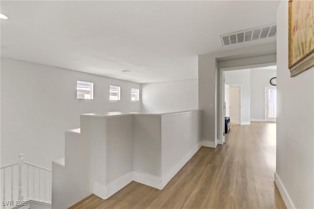 corridor featuring baseboards, visible vents, an upstairs landing, and wood finished floors