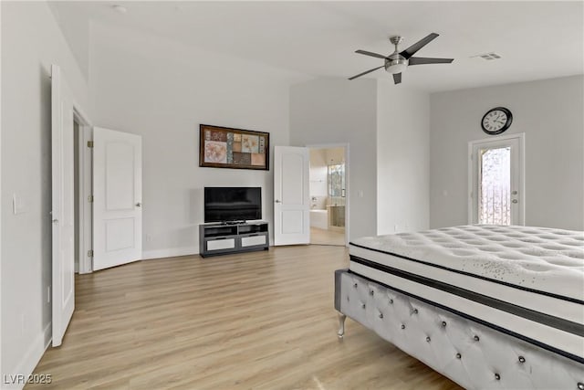 bedroom with light wood finished floors, visible vents, a towering ceiling, connected bathroom, and baseboards