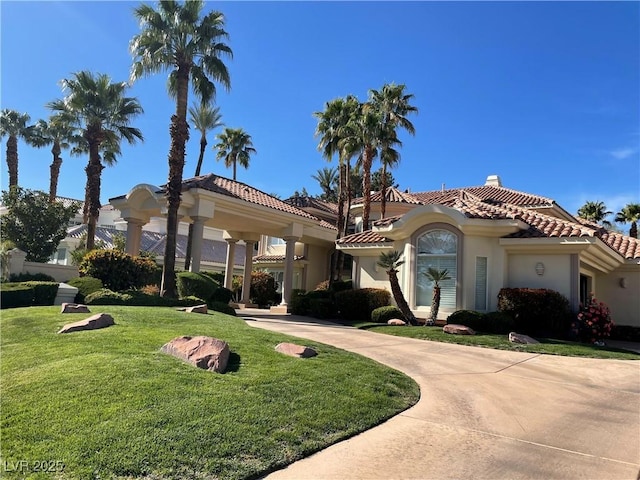 mediterranean / spanish-style home with concrete driveway, a tile roof, a chimney, a front lawn, and stucco siding