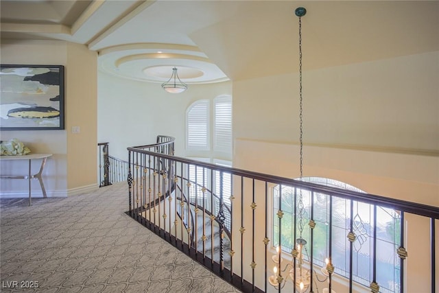 hallway with a tray ceiling, baseboards, carpet flooring, and an upstairs landing