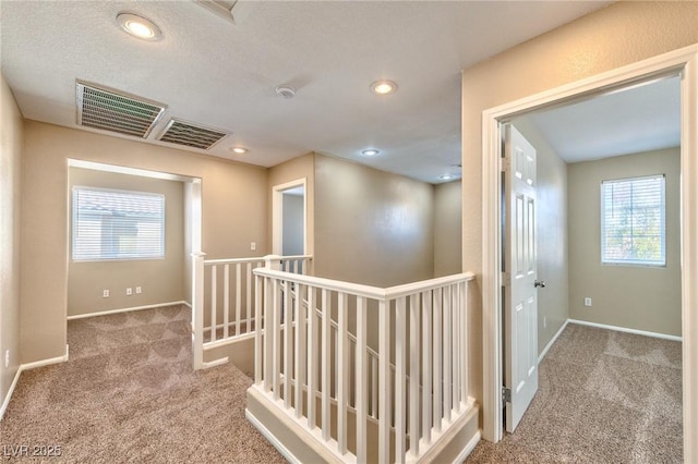 corridor featuring carpet, visible vents, and an upstairs landing