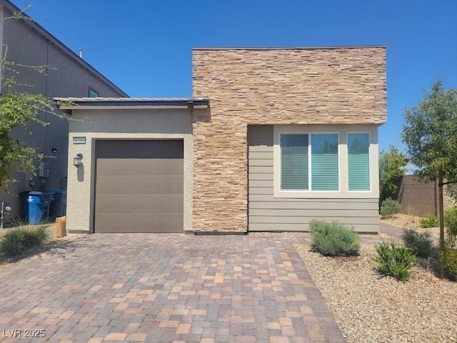 view of front of house featuring decorative driveway, stone siding, and an attached garage