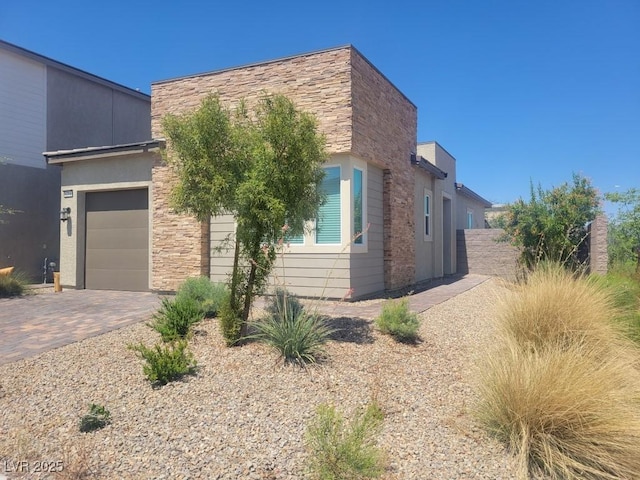 view of front facade featuring decorative driveway, stone siding, and an attached garage