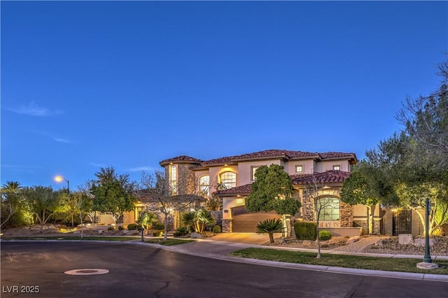 mediterranean / spanish house featuring stucco siding, concrete driveway, an attached garage, stone siding, and a tiled roof