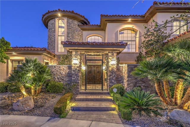 view of exterior entry featuring stone siding, a tile roof, and stucco siding