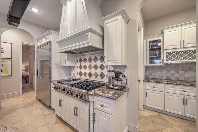 kitchen with custom range hood, white cabinetry, stainless steel appliances, and arched walkways