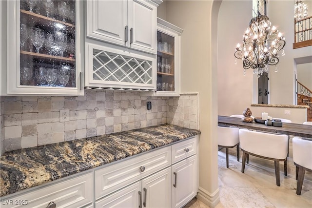 kitchen with arched walkways, hanging light fixtures, glass insert cabinets, and white cabinetry