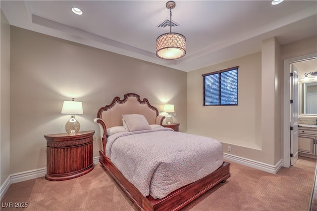 bedroom with a tray ceiling, visible vents, light carpet, ensuite bath, and baseboards