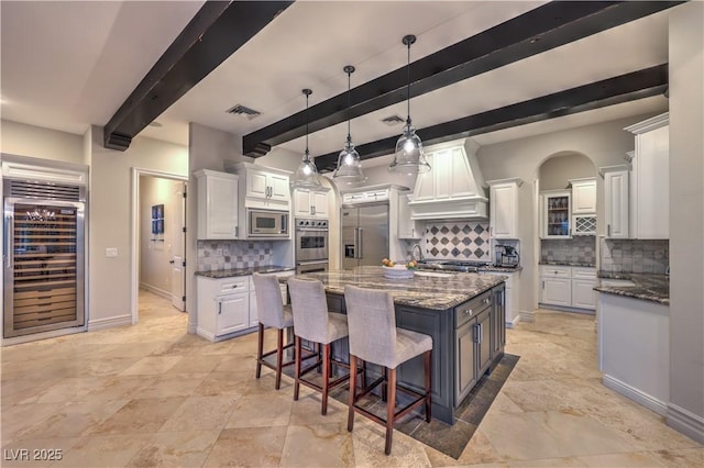 kitchen featuring beverage cooler, a kitchen island, dark stone countertops, built in appliances, and premium range hood