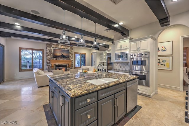 kitchen featuring a center island with sink, appliances with stainless steel finishes, white cabinets, a sink, and dark stone countertops