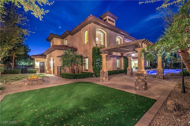 back of house at night featuring an outdoor fire pit, a patio, a tiled roof, a yard, and a pergola