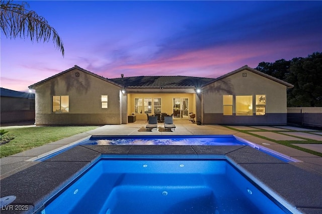 back of property at dusk featuring an outdoor pool, a patio area, fence, and stucco siding