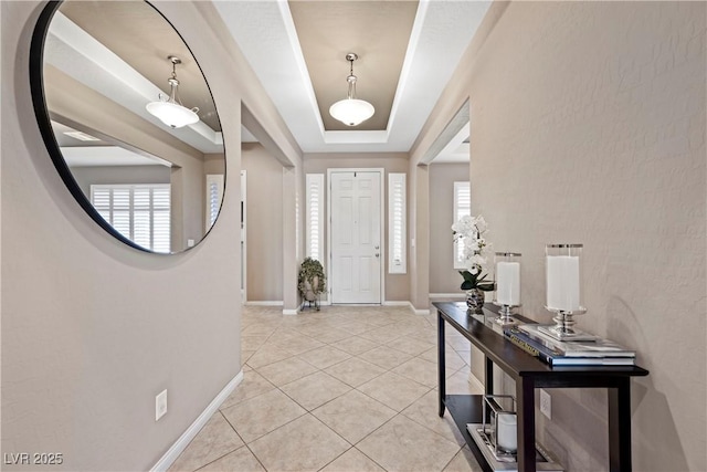 entryway with light tile patterned floors, baseboards, and a tray ceiling