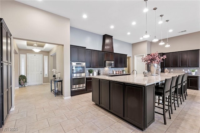 kitchen with a spacious island, stainless steel appliances, hanging light fixtures, backsplash, and dark brown cabinetry