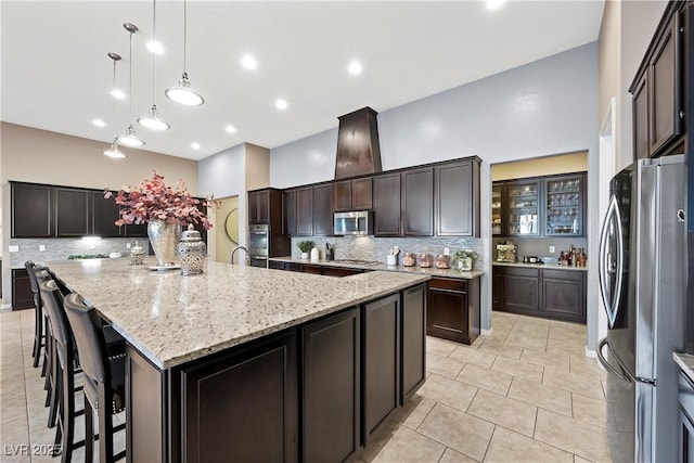 kitchen with appliances with stainless steel finishes, decorative light fixtures, a large island with sink, and dark brown cabinetry