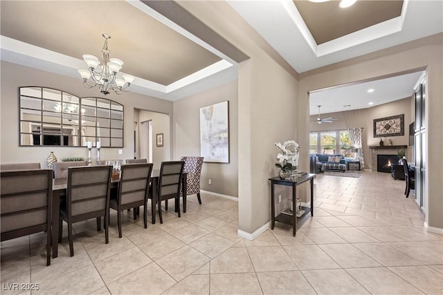 dining area featuring light tile patterned floors, a warm lit fireplace, and a raised ceiling