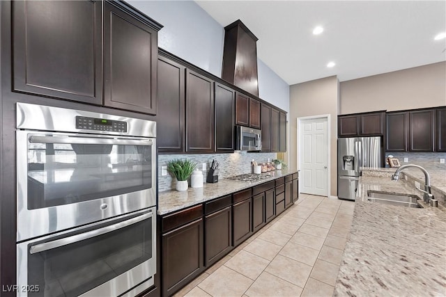 kitchen with light stone counters, a sink, dark brown cabinets, appliances with stainless steel finishes, and backsplash