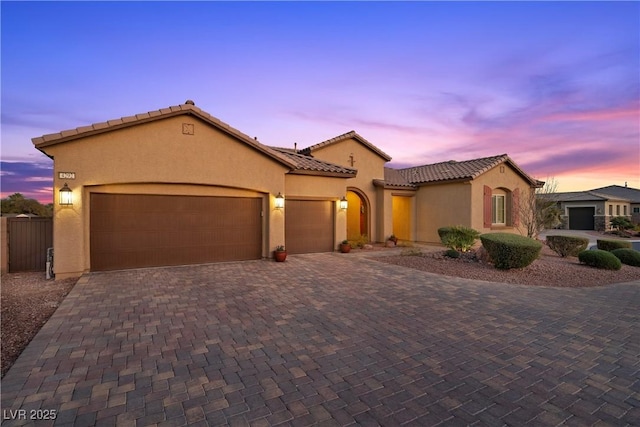 mediterranean / spanish-style house with a garage, decorative driveway, a tile roof, and stucco siding