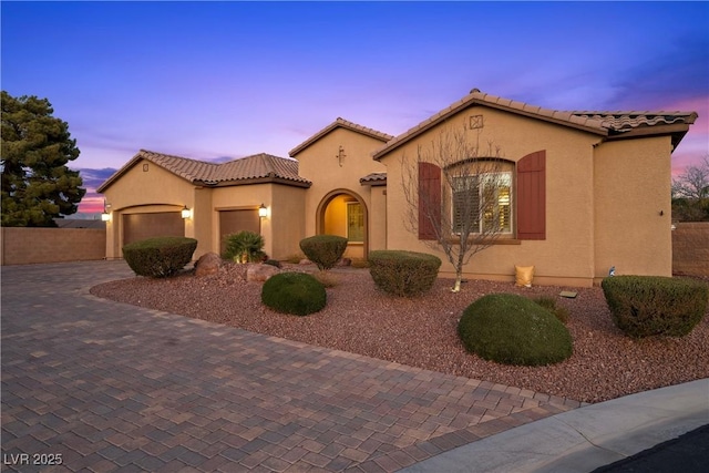 mediterranean / spanish home with a garage, a tiled roof, decorative driveway, and stucco siding