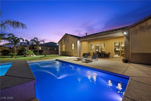 pool at dusk featuring a patio area, fence, and an outdoor pool