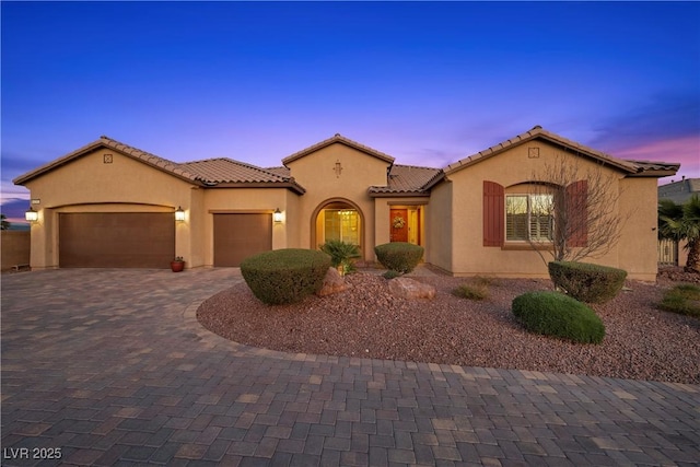 mediterranean / spanish-style home with a garage, decorative driveway, and stucco siding