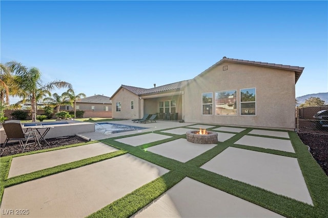 rear view of house with a tile roof, a patio, stucco siding, an outdoor fire pit, and an outdoor pool