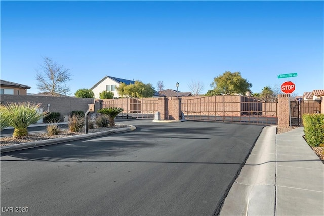 view of road featuring street lights, curbs, a gated entry, and a gate