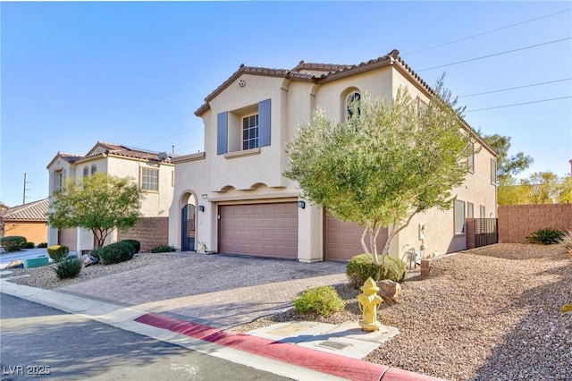 mediterranean / spanish house with a tiled roof, an attached garage, fence, decorative driveway, and stucco siding