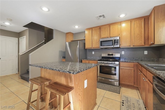 kitchen featuring light tile patterned flooring, stainless steel appliances, a kitchen island, visible vents, and a kitchen bar