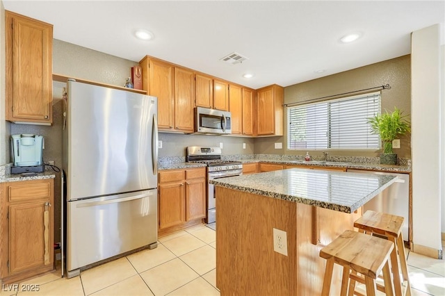 kitchen featuring light tile patterned floors, a kitchen island, light stone counters, a kitchen breakfast bar, and stainless steel appliances