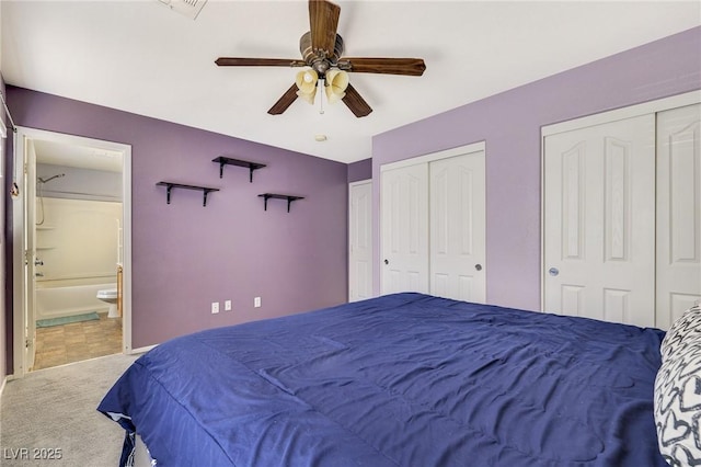 carpeted bedroom with visible vents, two closets, a ceiling fan, baseboards, and ensuite bath