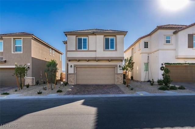 view of front of property featuring a garage, decorative driveway, stone siding, and stucco siding