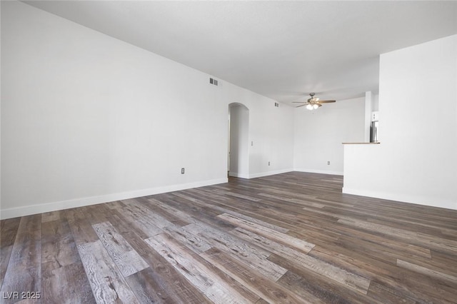 empty room with a ceiling fan, visible vents, arched walkways, and dark wood-type flooring