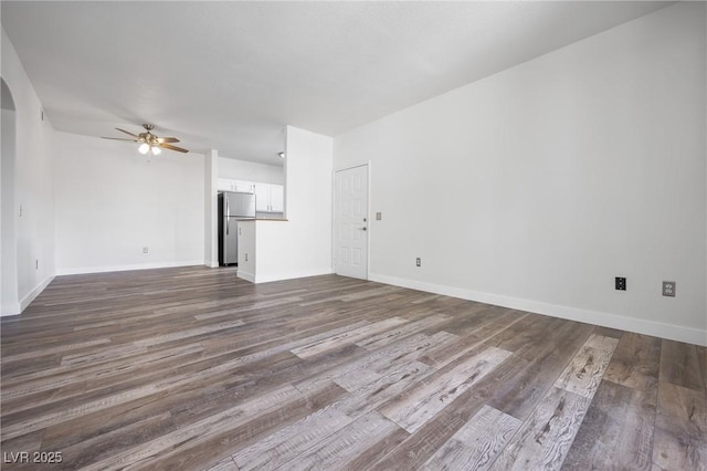 unfurnished living room with baseboards, arched walkways, ceiling fan, and dark wood-style flooring