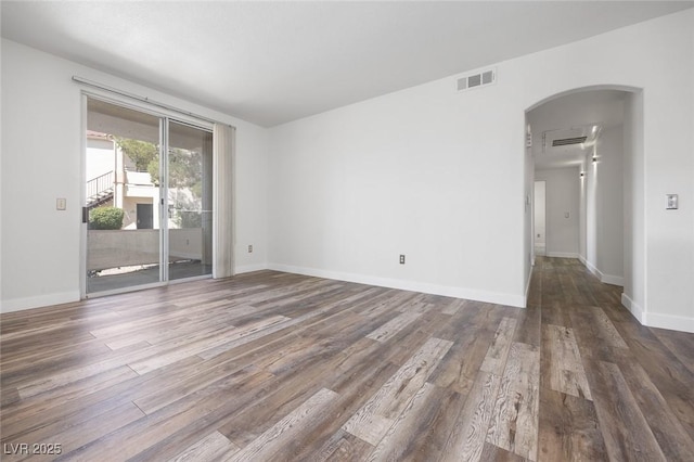 empty room with wood finished floors, arched walkways, baseboards, and visible vents