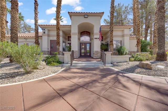 view of front facade featuring french doors, a tiled roof, stucco siding, and stone siding
