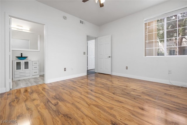 unfurnished bedroom featuring baseboards, ensuite bath, ceiling fan, visible vents, and wood finished floors